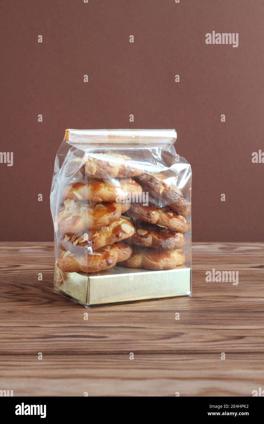 Shortbread-Kekse mit Mandelflocken in transparentem Beutel auf einem Holztisch gegen braune Wand. Nahaufnahme Stockfoto