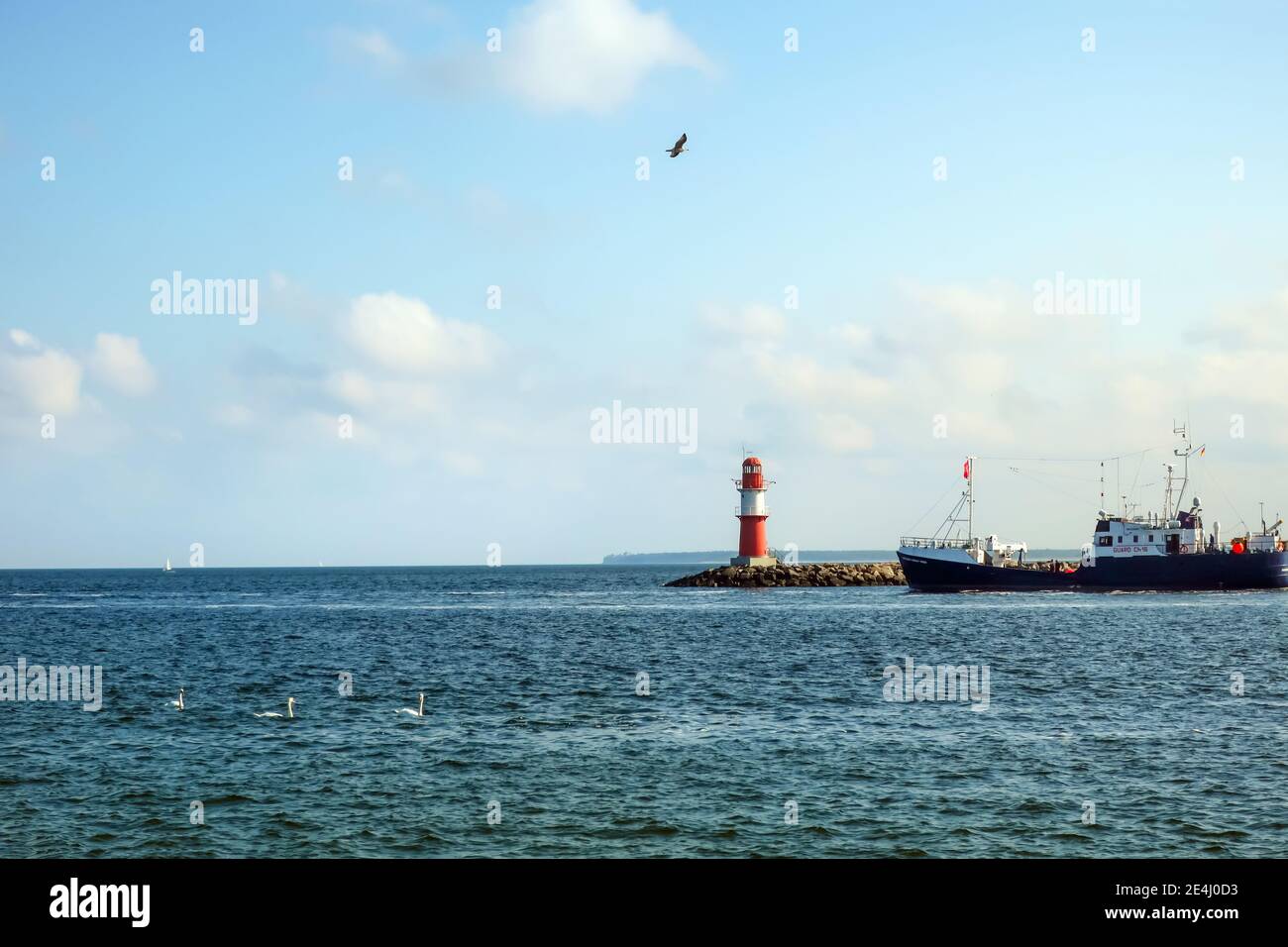 Ein rot-weißer Leuchtturm am Horizont von der Uferpromenade am Hafen von Warnemunde Rostock an der Ostsee. Stockfoto
