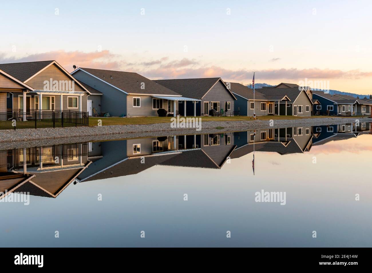 Eine Reihe ähnlicher Häuser in einer Unterteilung am Wasser spiegeln sich entlang eines glatten Sees. Stockfoto
