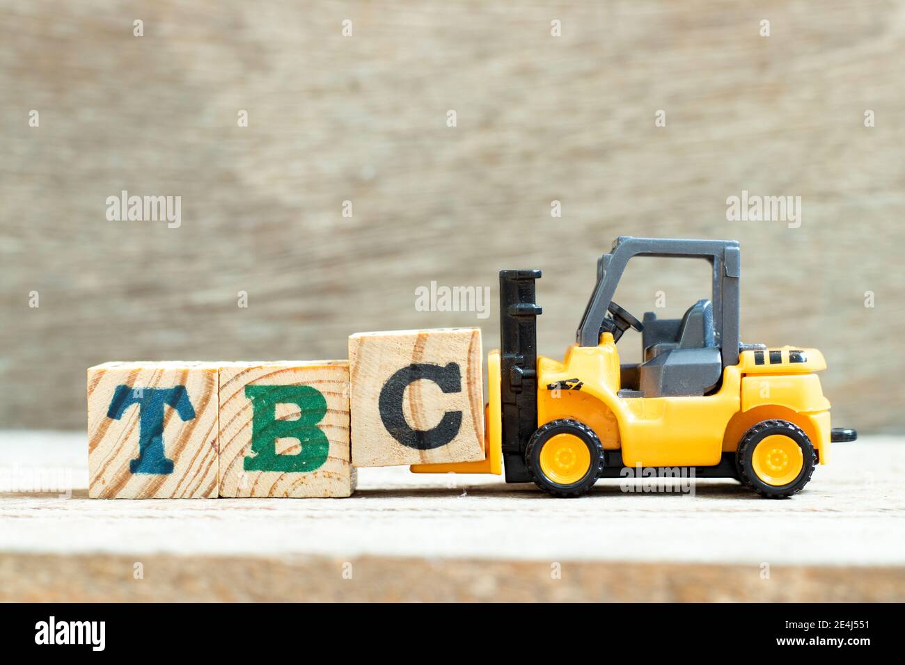 Spielzeug Gabelstapler halten Buchstabenblock c, um Wort TBC abzuschließen (Abkürzung von muss bestätigt oder fortgesetzt werden) auf Holzhintergrund Stockfoto