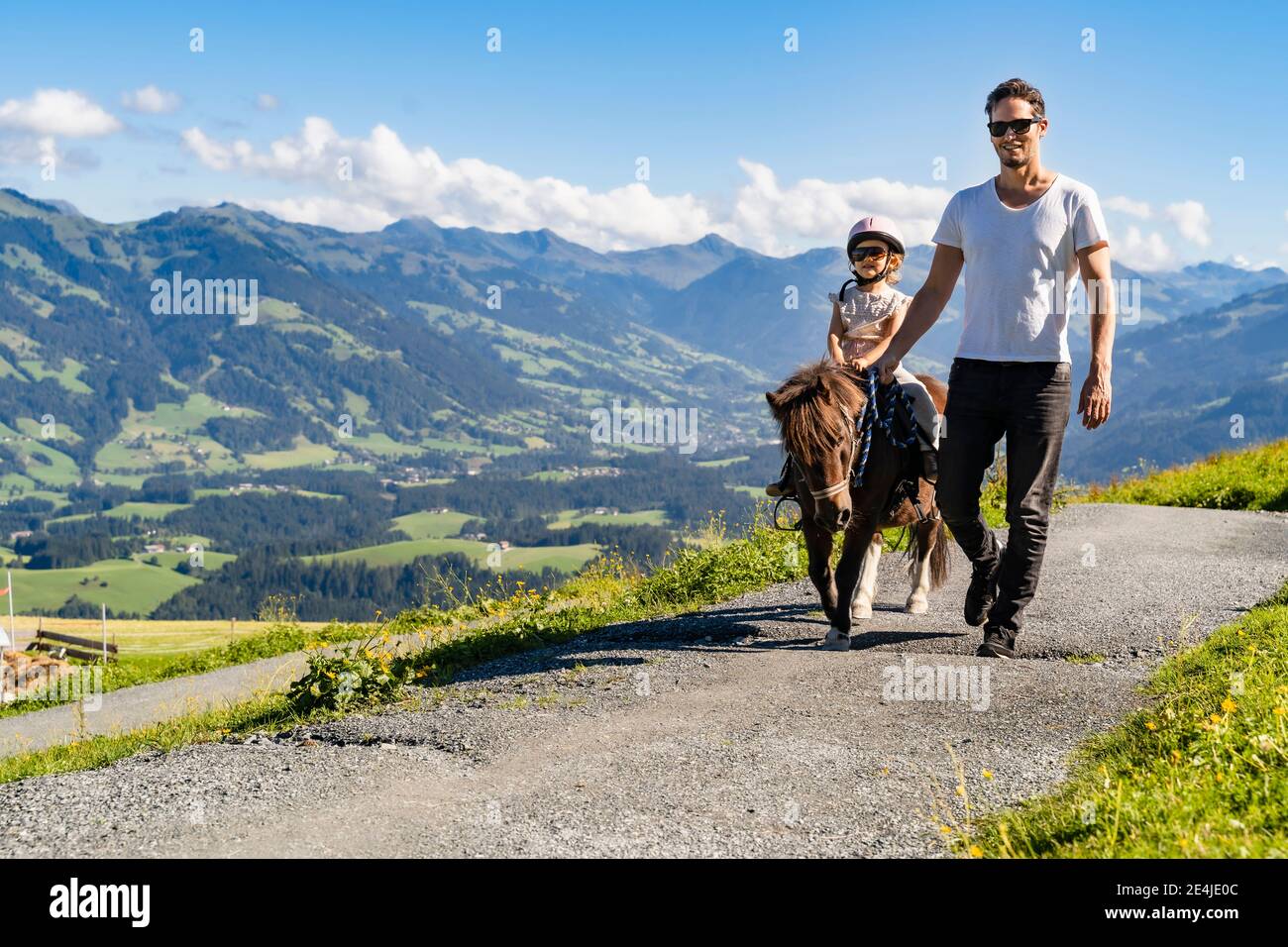 Vater geht neben der kleinen Tochter auf dem Pony auf dem alpinen Wanderweg Stockfoto