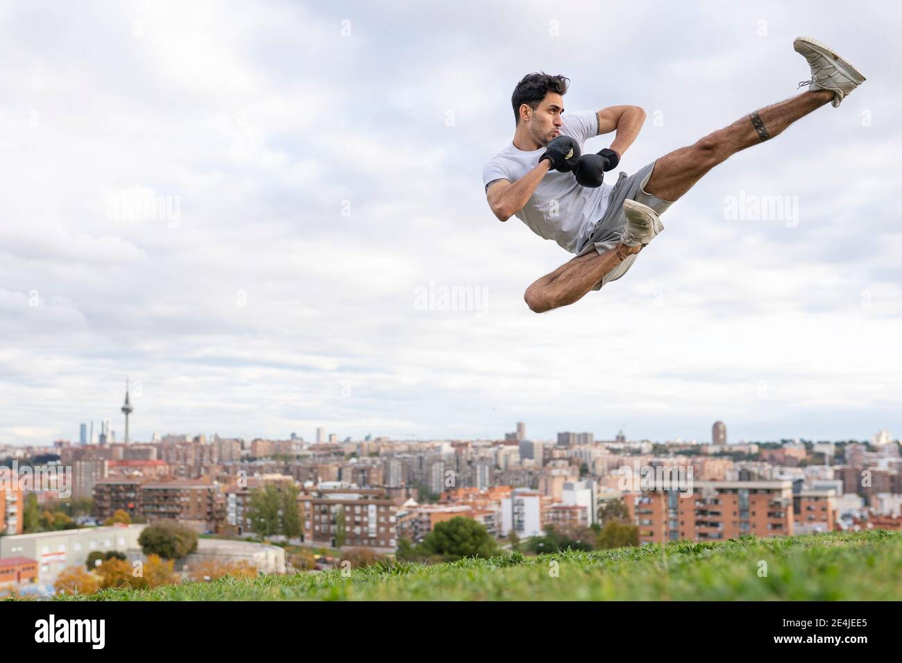 Junger männlicher akrobaten übt Kickboxen in der Luft auf Hügel in Stadt Stockfoto