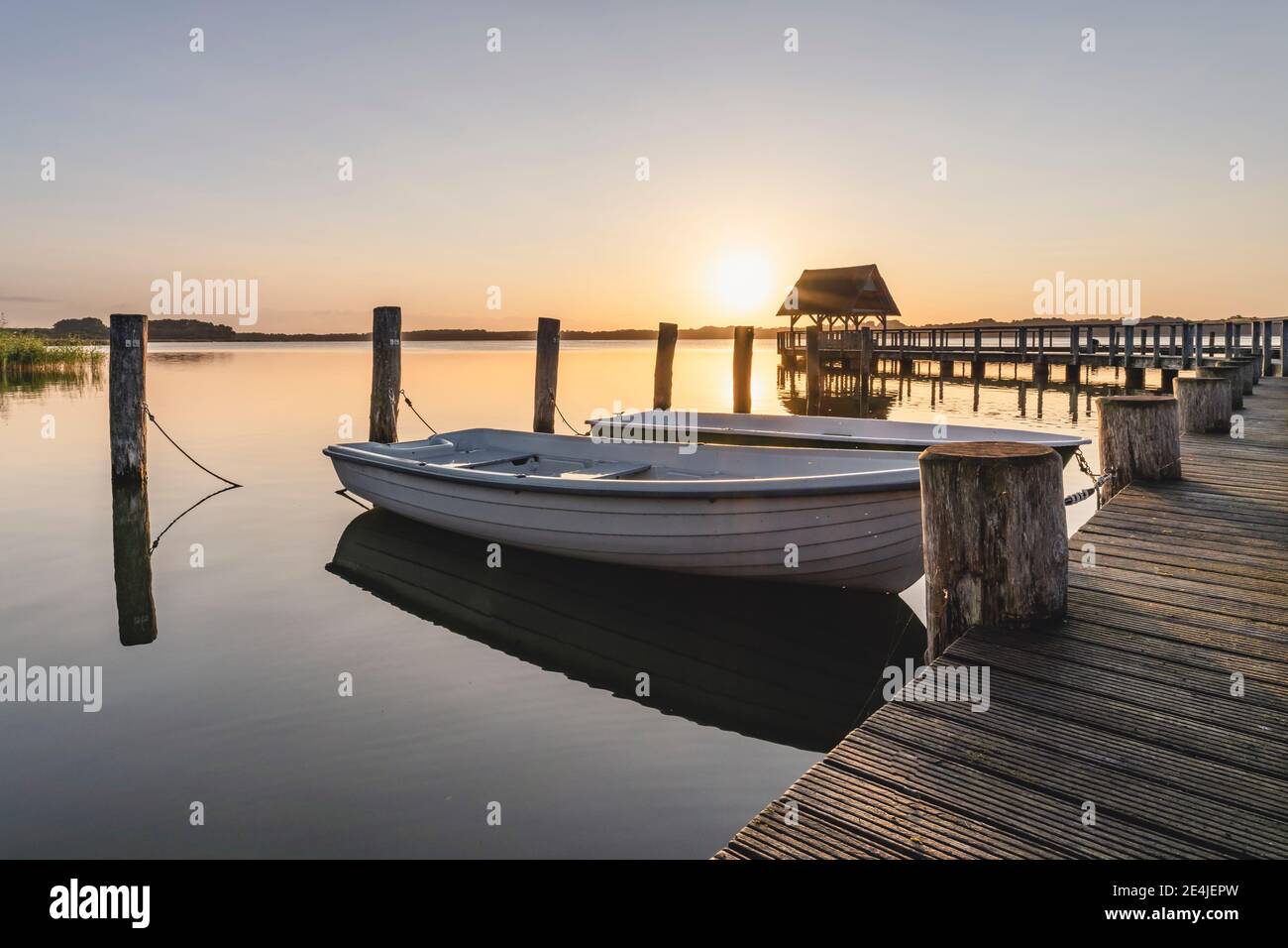 Deutschland, Schleswig-Holstein, Hemmelsdorf, Ruderboote am Steg am Hemmelsdorfer See bei Sonnenaufgang Stockfoto