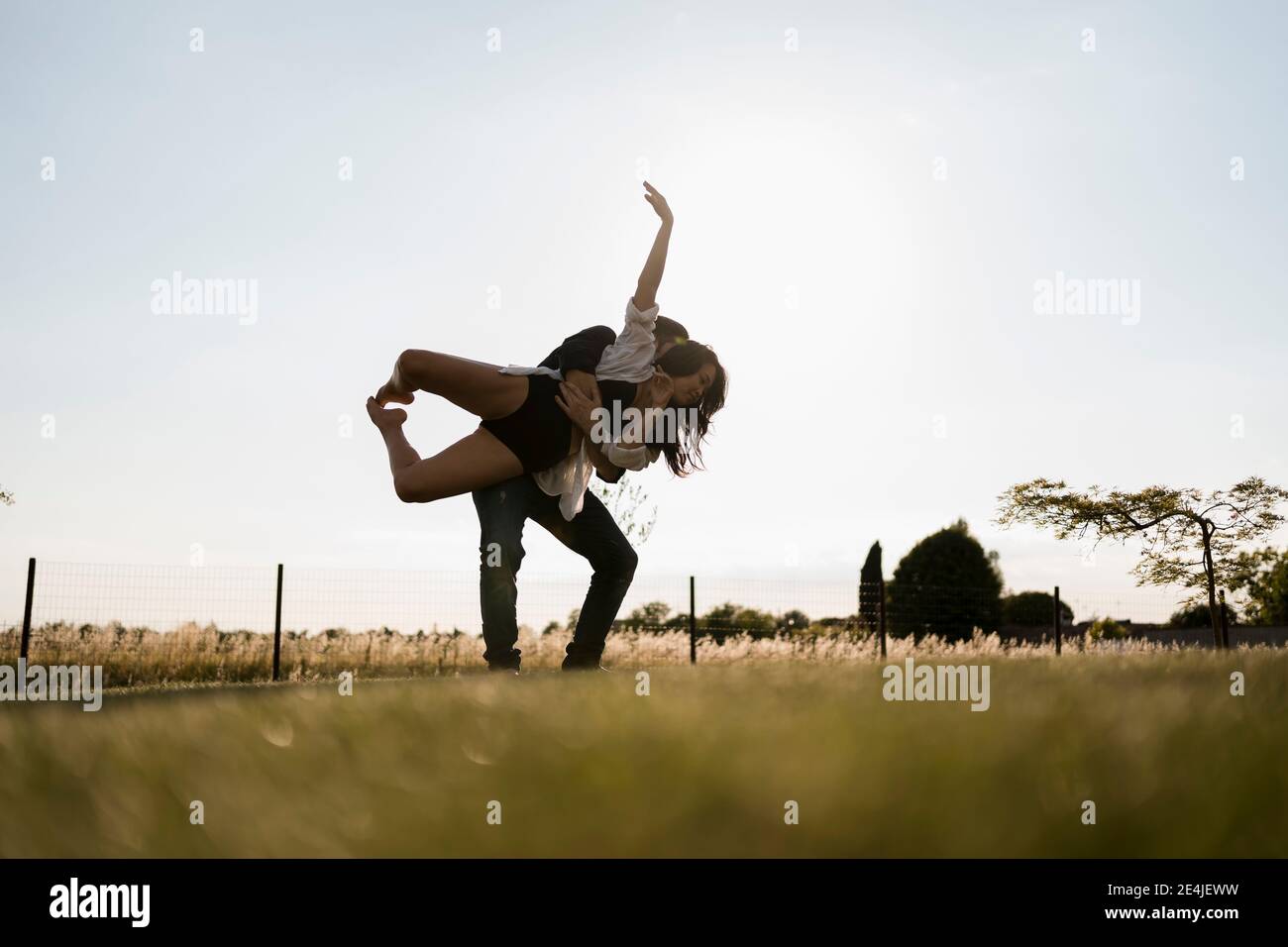 Männliche Tänzerin nimmt weibliche Tänzerin auf, während sie auf dem Feld gegen den klaren Himmel tanzt Stockfoto
