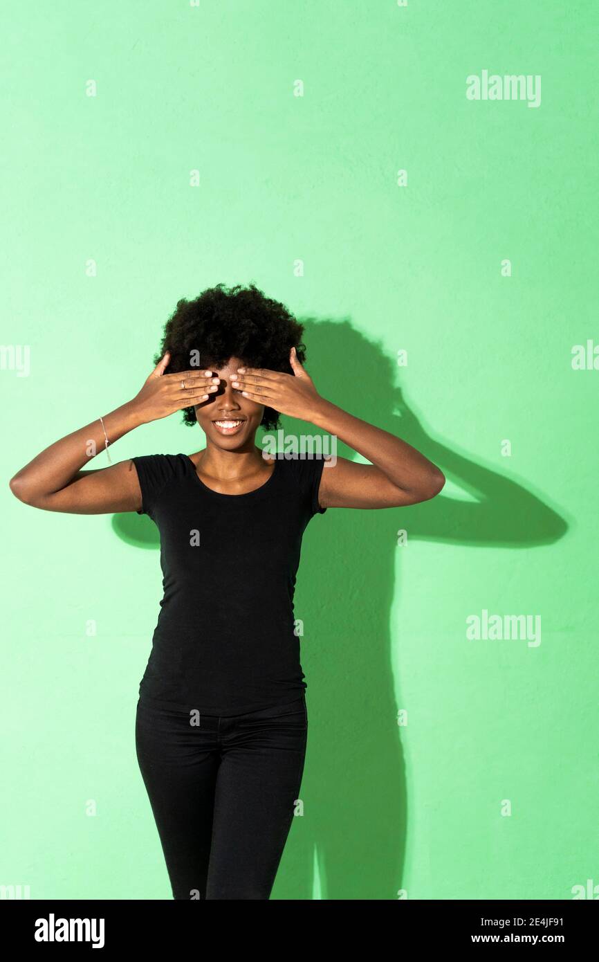 Frau, die die Augen bedeckt, während sie vor grünem Hintergrund steht Stockfoto