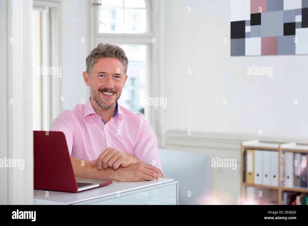 Lächelnder reifer männlicher Profi am Laptop am Schreibtisch im Büro Hütte Stockfoto Lächelnder reifer männlicher Profi am Laptop am Schreibtisch im Büro Hütte Stockfoto