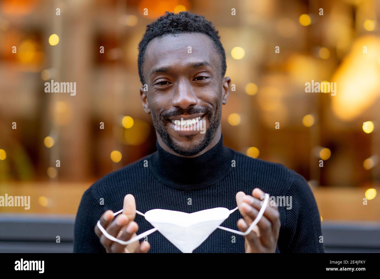 Lächelnder Mann hält eine schützende Gesichtsmaske, während er im Freien steht Stockfoto