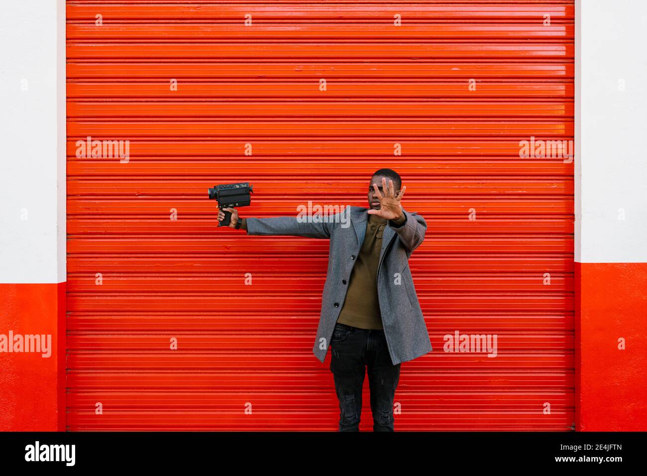 Mann mit alter Filmkamera, die im Stehen Stop-Geste zeigt Gegen rote Wand Stockfoto
