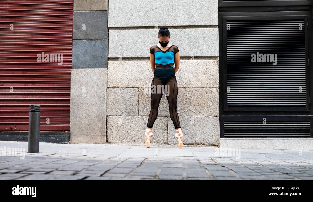Balletttänzerin trägt schützende Gesichtsmaske stehend Zehenspitzen mit Händen Hinter dem Kopf auf dem Fußweg während der COVID-19 Stockfoto