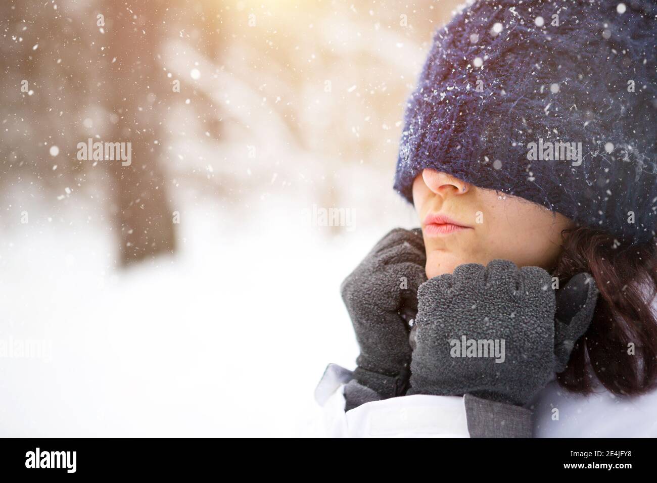 Frau mit gestricktem Hut zog kalt über die Augen und wärmt ihre Hände mit ihrem Atem. Outdoor-Aktivitäten, Frühling, Winter, Schnee schmilzt, Schneefall, f Stockfoto