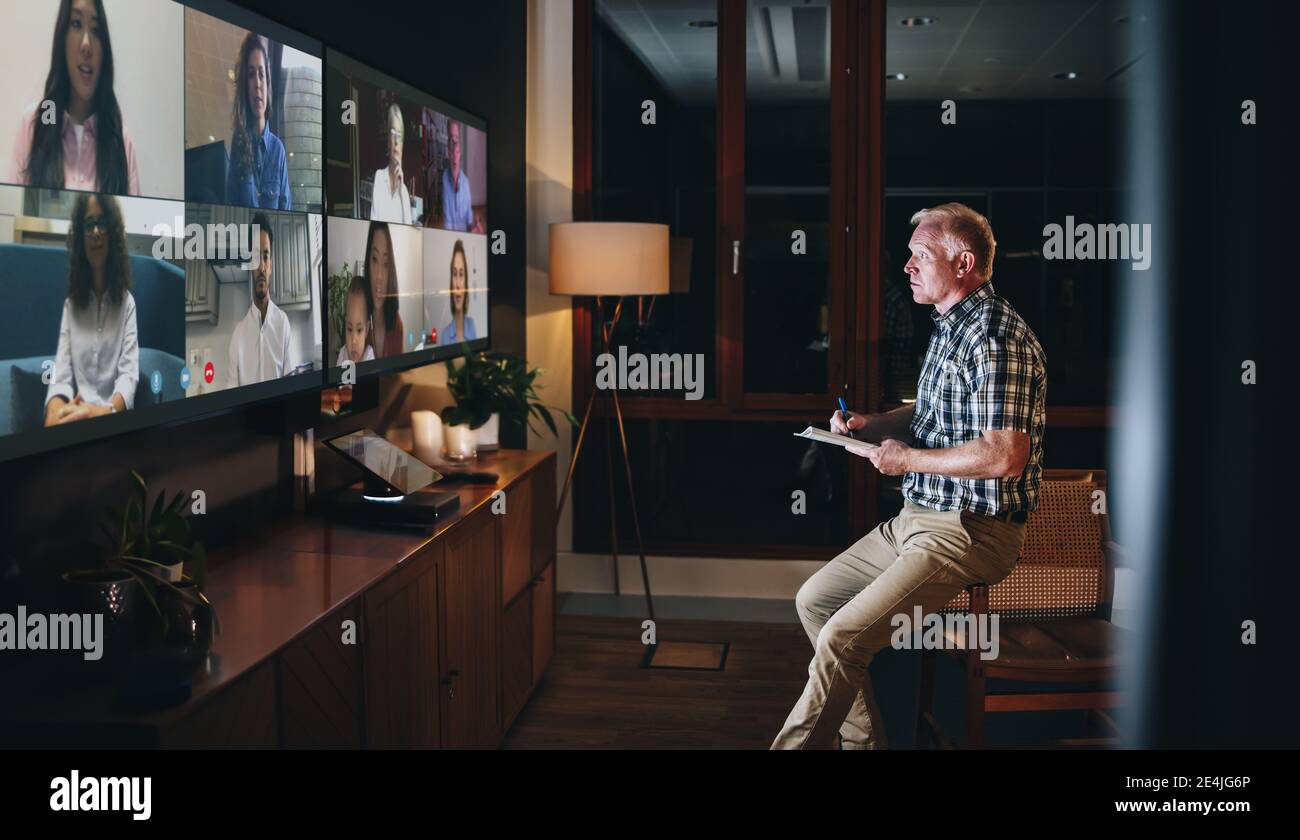 Online-Besprechung des Geschäftsteams über einen Videoanruf. Ein Mann sitzt im Sitzungssaal im Büro und hat nachts eine Videokonferenz mit seinen Kollegen. Stockfoto