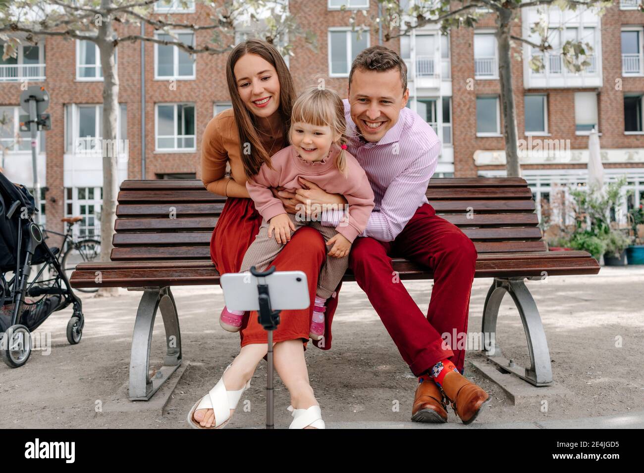 Glückliche Familie mit einer Tochter, die Selfie vom Handy aus sprach Auf Stativ an Parkbank Stockfoto Glückliche Familie mit einer Tochter, die Selfie vom Handy aus sprach Auf Stativ an Parkbank Stockfoto