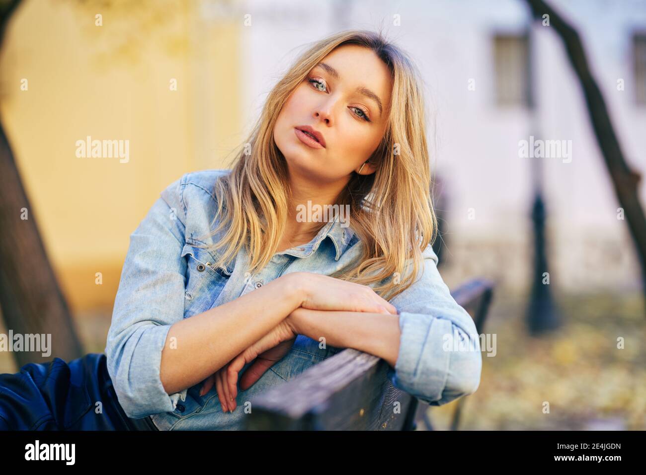 Blonde Frau trägt Jeanshemd und schwarzen Lederrock sitzen in einer städtischen Bank. Stockfoto
