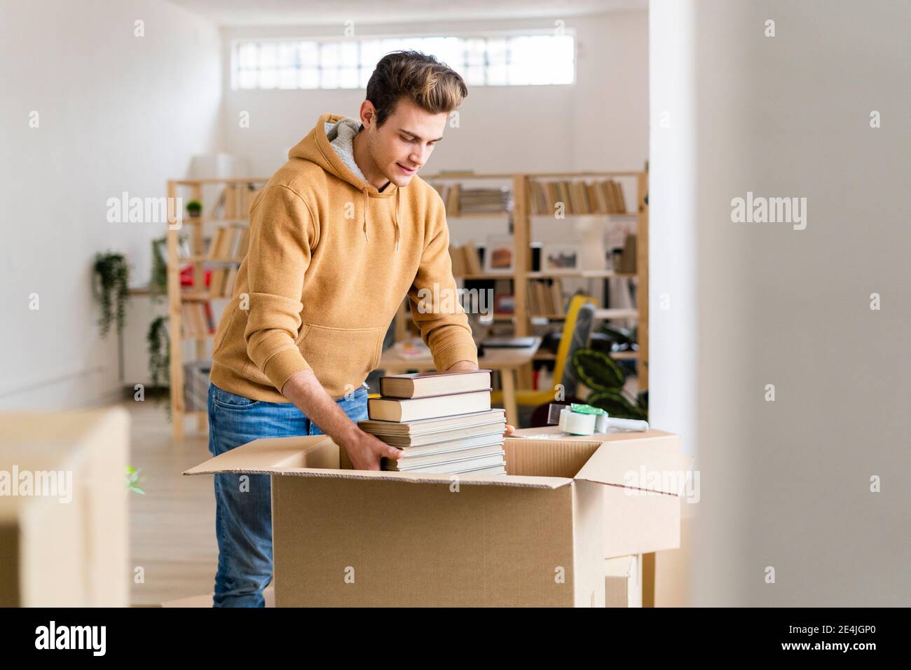 Junger Mann, der Bücher in Pappkarton in einem neuen Loft verpackt Wohnung Stockfoto
