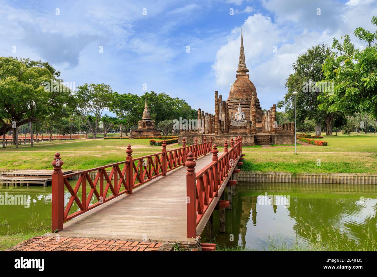 Rote Holzbrücke über den Teich, die zur Pagode und ruinierten Kapelle Kloster Komplex im Wat Sa Si Tempel, Sukhothai Historical Park, Thailand Stockfoto