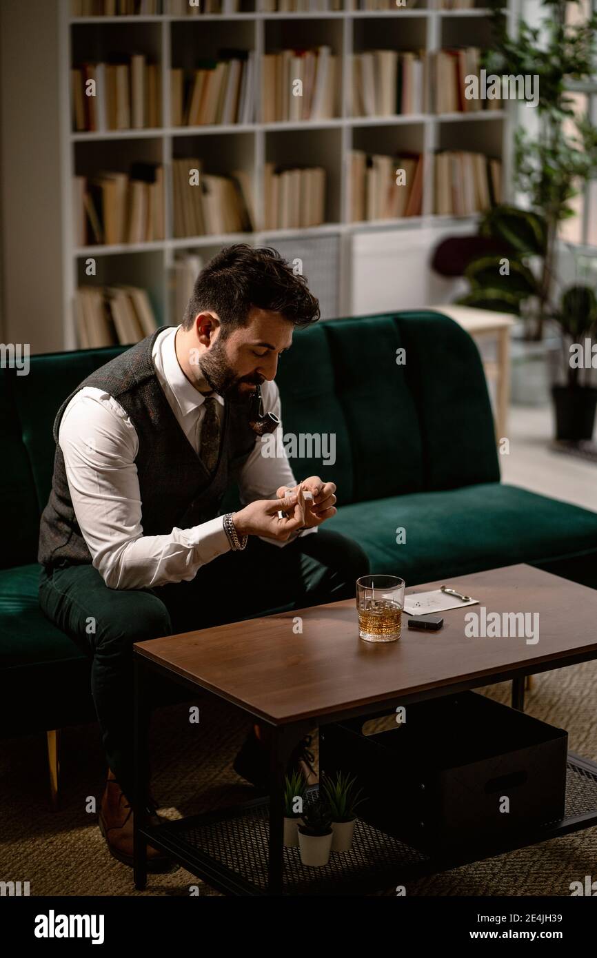Bärtiger Mann, der auf dem Sofa sitzt und Rauchpfeife vorbereitet Stockfoto