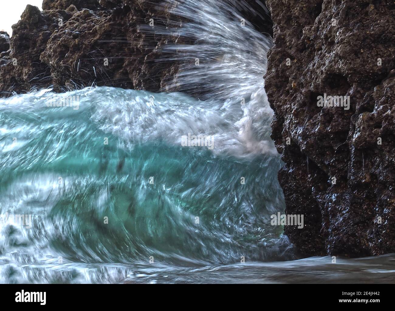 Grüne Wellen treffen in Zeitlupe auf eine Klippe Stockfoto