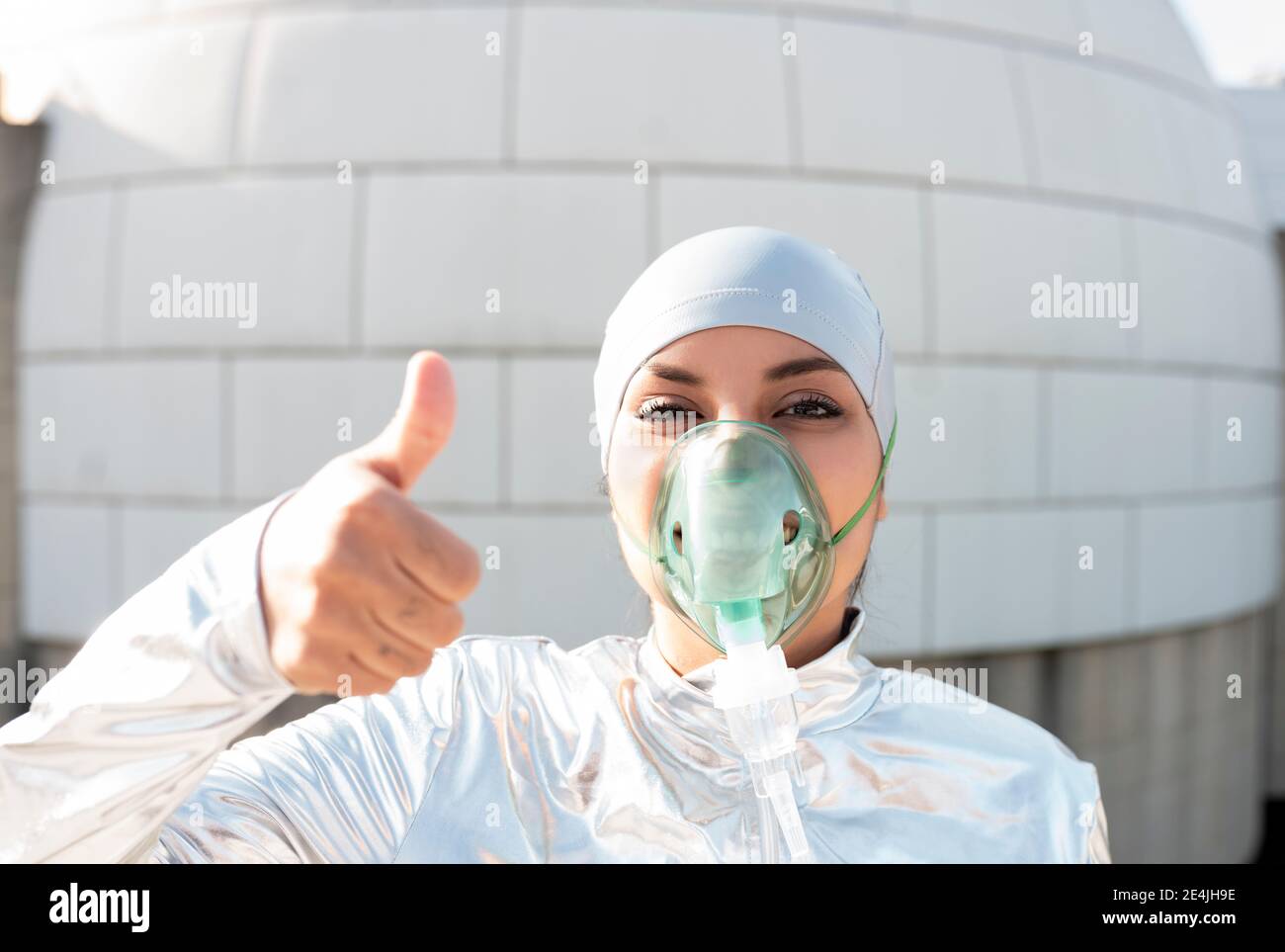 Junge Frau in Schutzanzug mit Sauerstoff-Gesichtsmaske und futuristischer Sonnenbrille mit Stop-Geste, während sie gegen Iglu steht Stockfoto