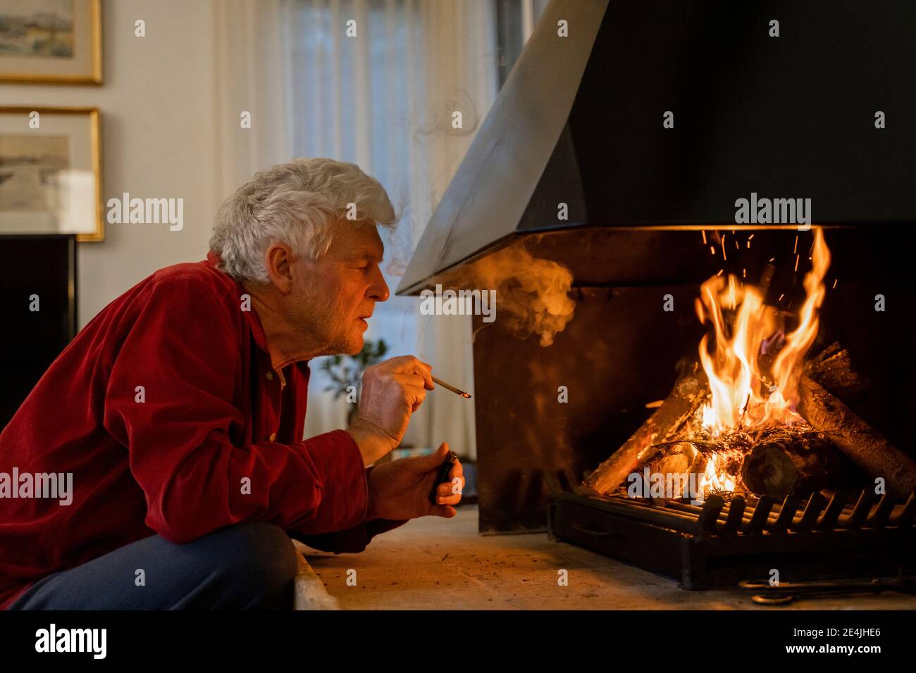 Mann, der Zigarette raucht, während er am Kamin zu Hause sitzt Stockfoto