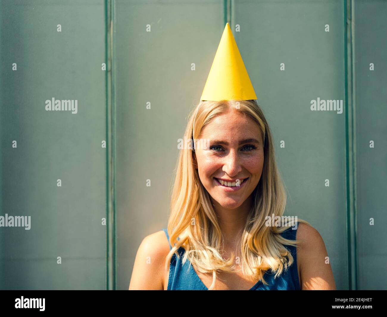 Lächelnde Frau mit Partyhut gegen graue Wand Stockfoto