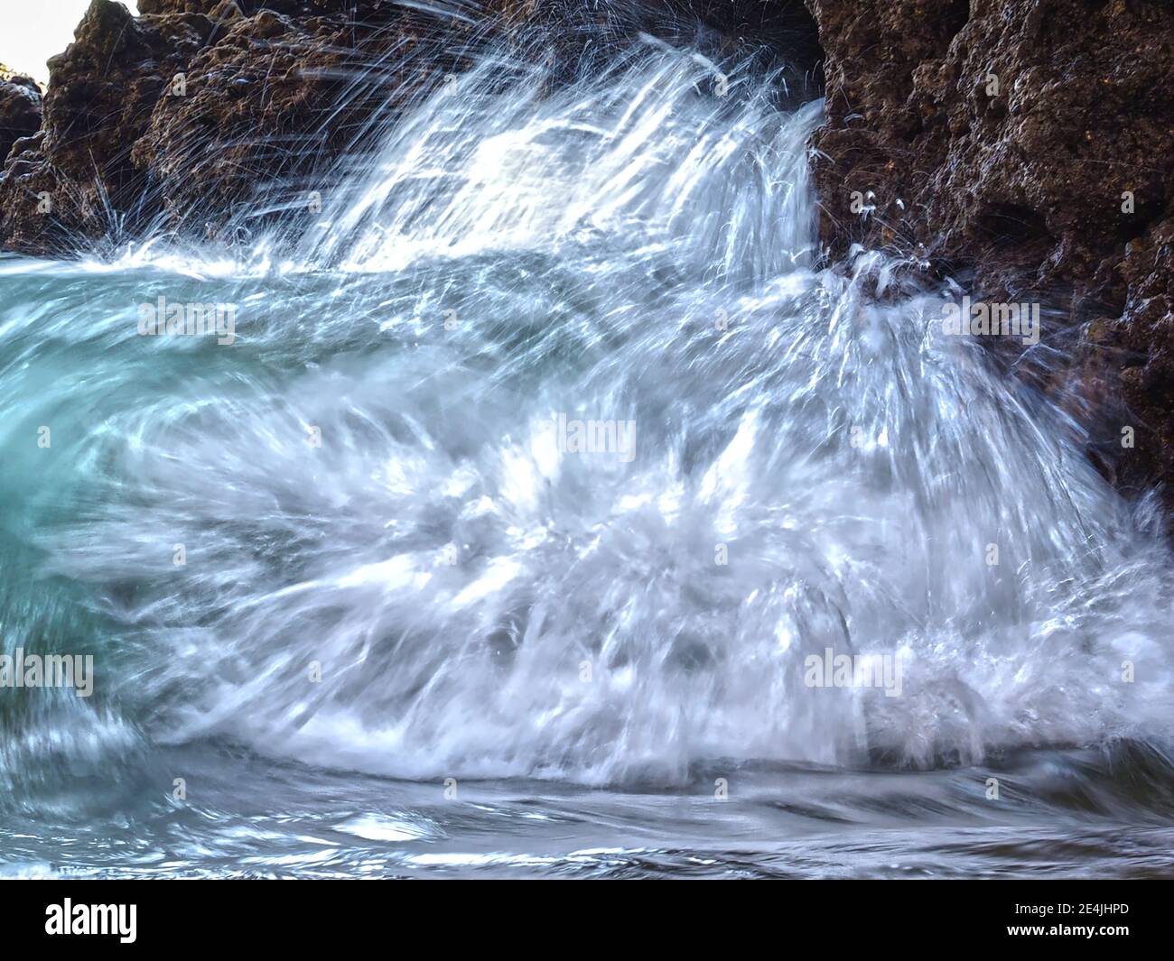 Grüne Wellen treffen in Zeitlupe auf eine Klippe Stockfoto