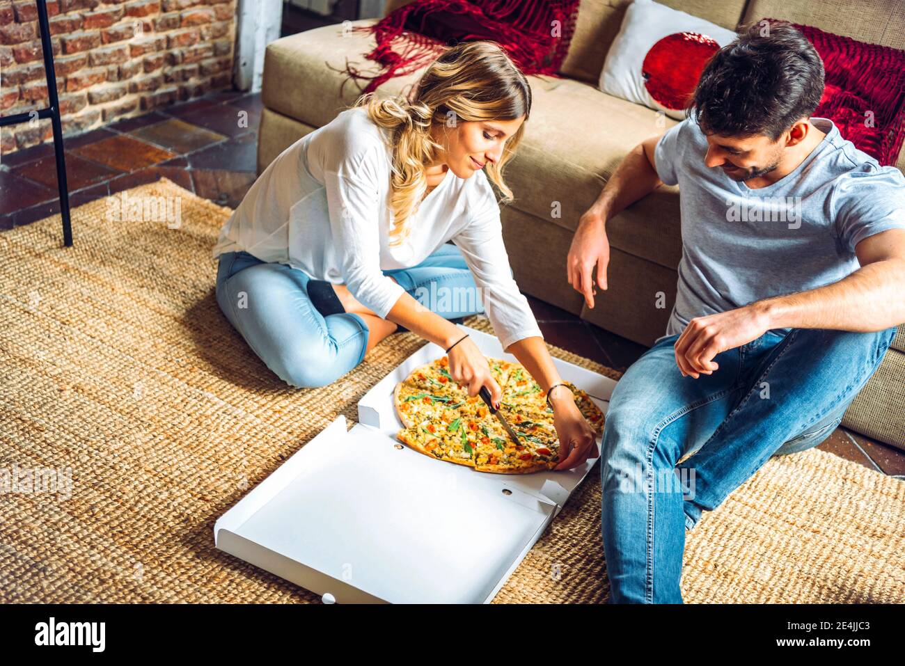 Junges Paar sitzt auf dem Boden des Wohnzimmers und Schneiden Pizza im Karton Stockfoto