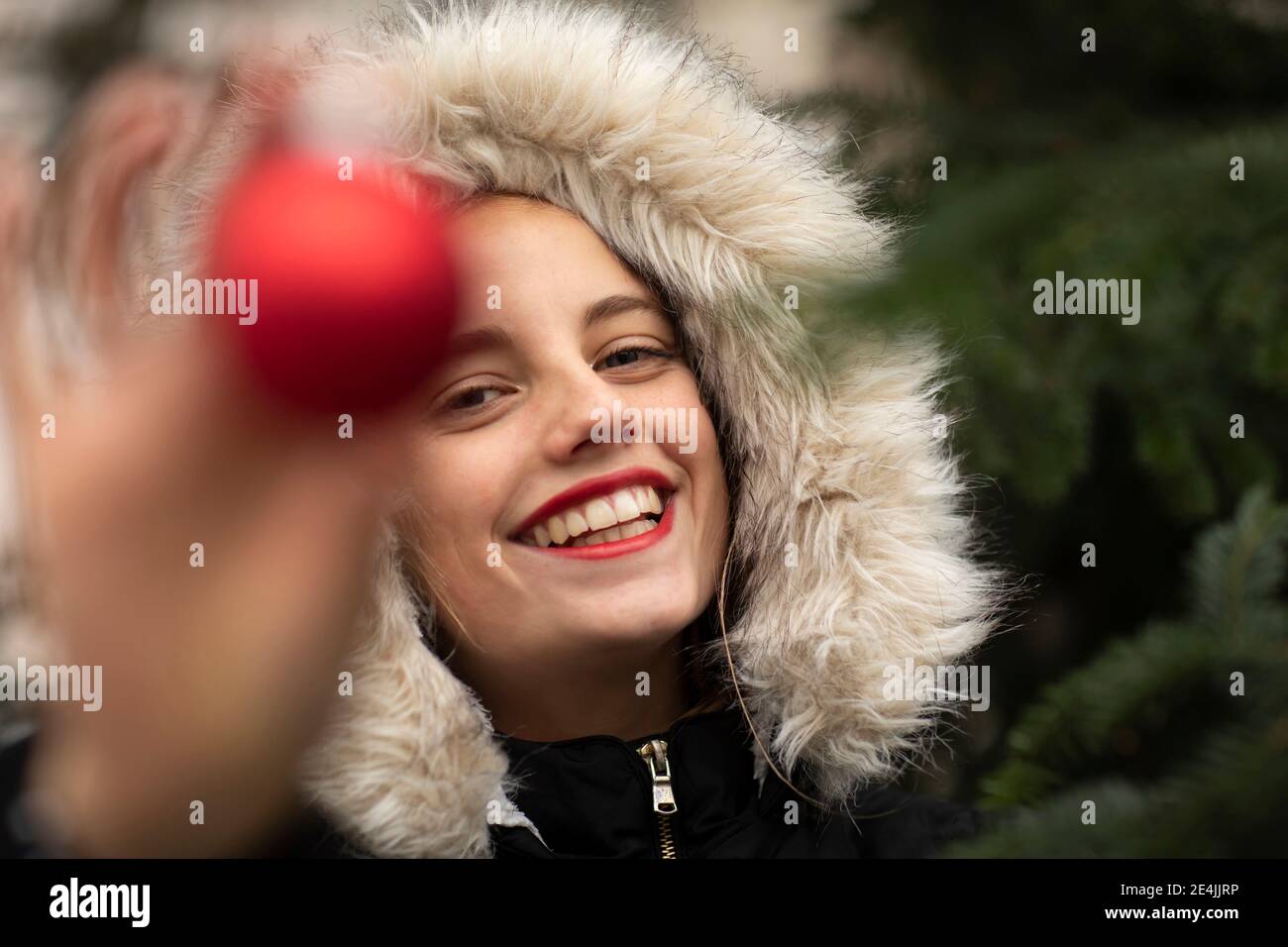 Fröhliche Frau in warmer Kleidung hält Weihnachtsschmuck bei Kälte Temperatur Stockfoto