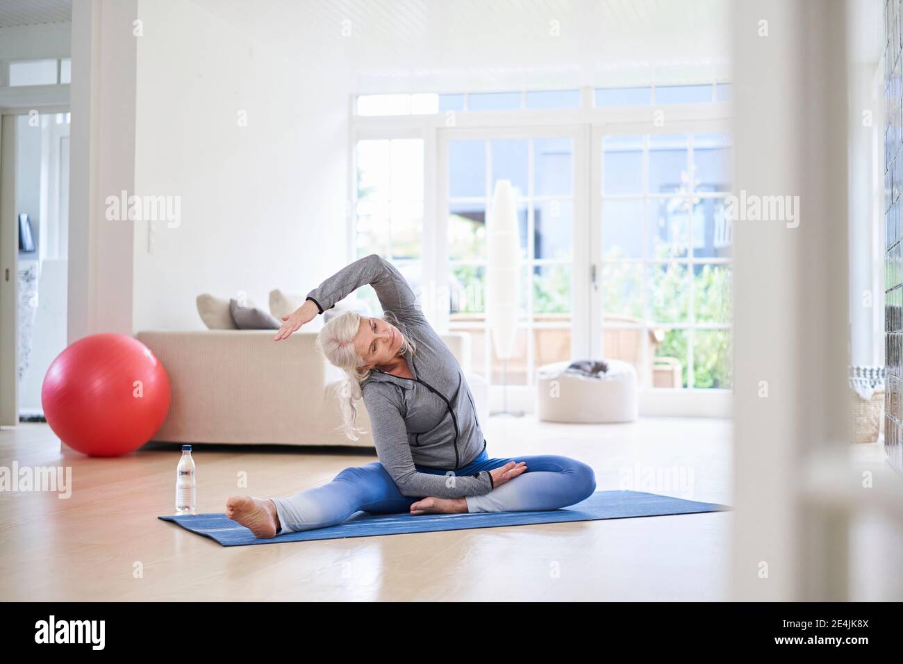 Ältere Frau, die beim Training im Wohnzimmer die Arme streckt Stockfoto