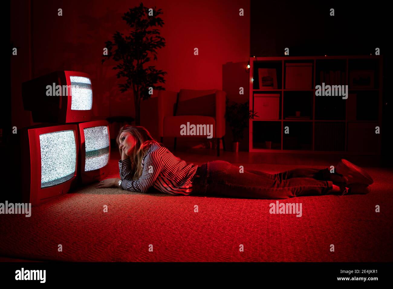 Junge Frau mit der Hand im Haar auf dem Boden liegend Vor alten Fernsehern im Wohnzimmer Stockfoto