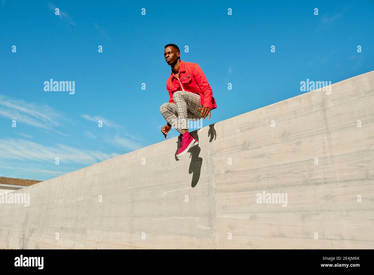 Junger Mann in roter Jacke und karierter Hose springt aus Betonwand Stockfoto