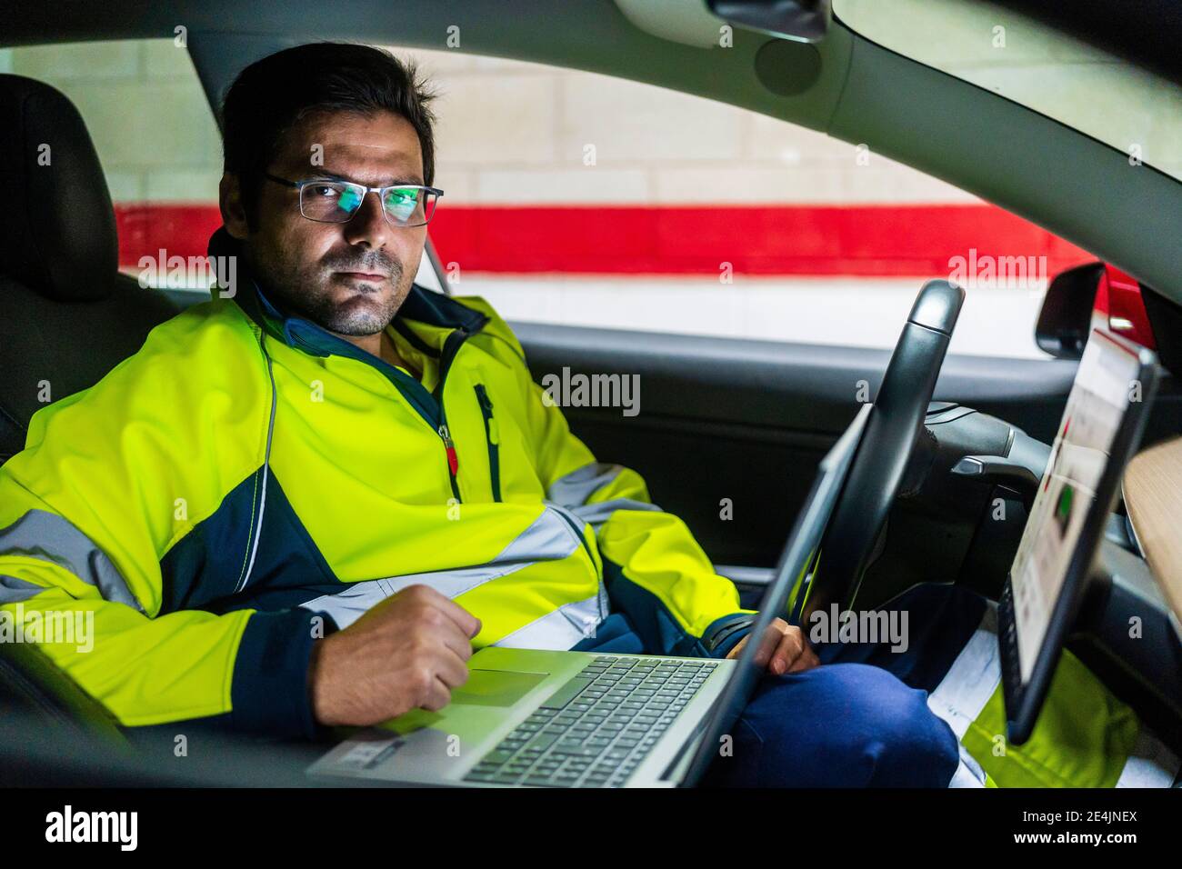 Professioneller Techniker mit Laptop, der im Elektroauto im Auto arbeitet Reparaturwerkstatt Stockfoto