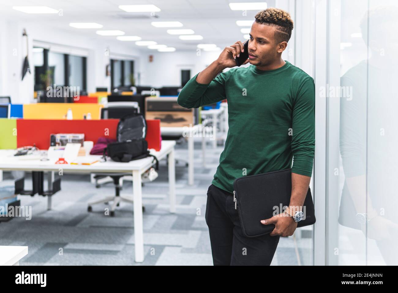 Männlicher Profi mit Aktendokument auf Telefonanruf stützend auf Glas am Arbeitsplatz Stockfoto
