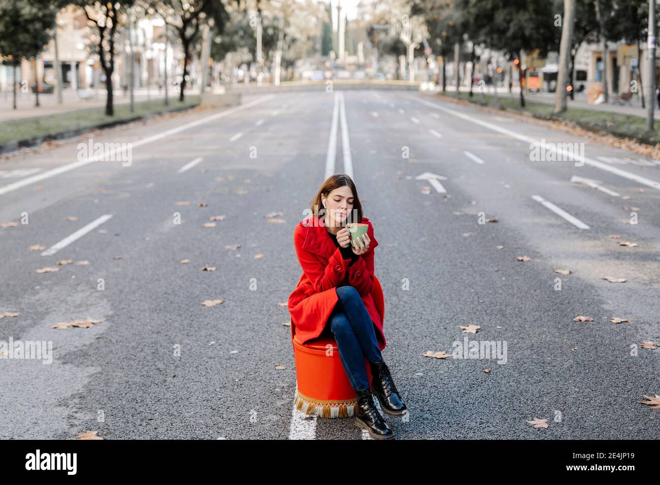 Modische junge Frau hält Kaffeetasse, während Musik mit hören Augen auf der Straße geschlossen Stockfoto