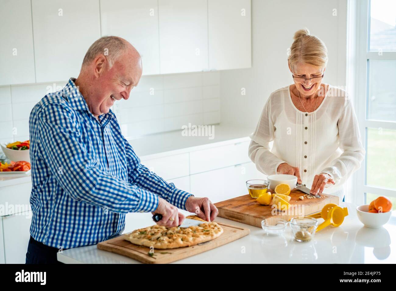 Seniorenpaar schneidet Essen auf Kücheninsel zu Hause Stockfoto