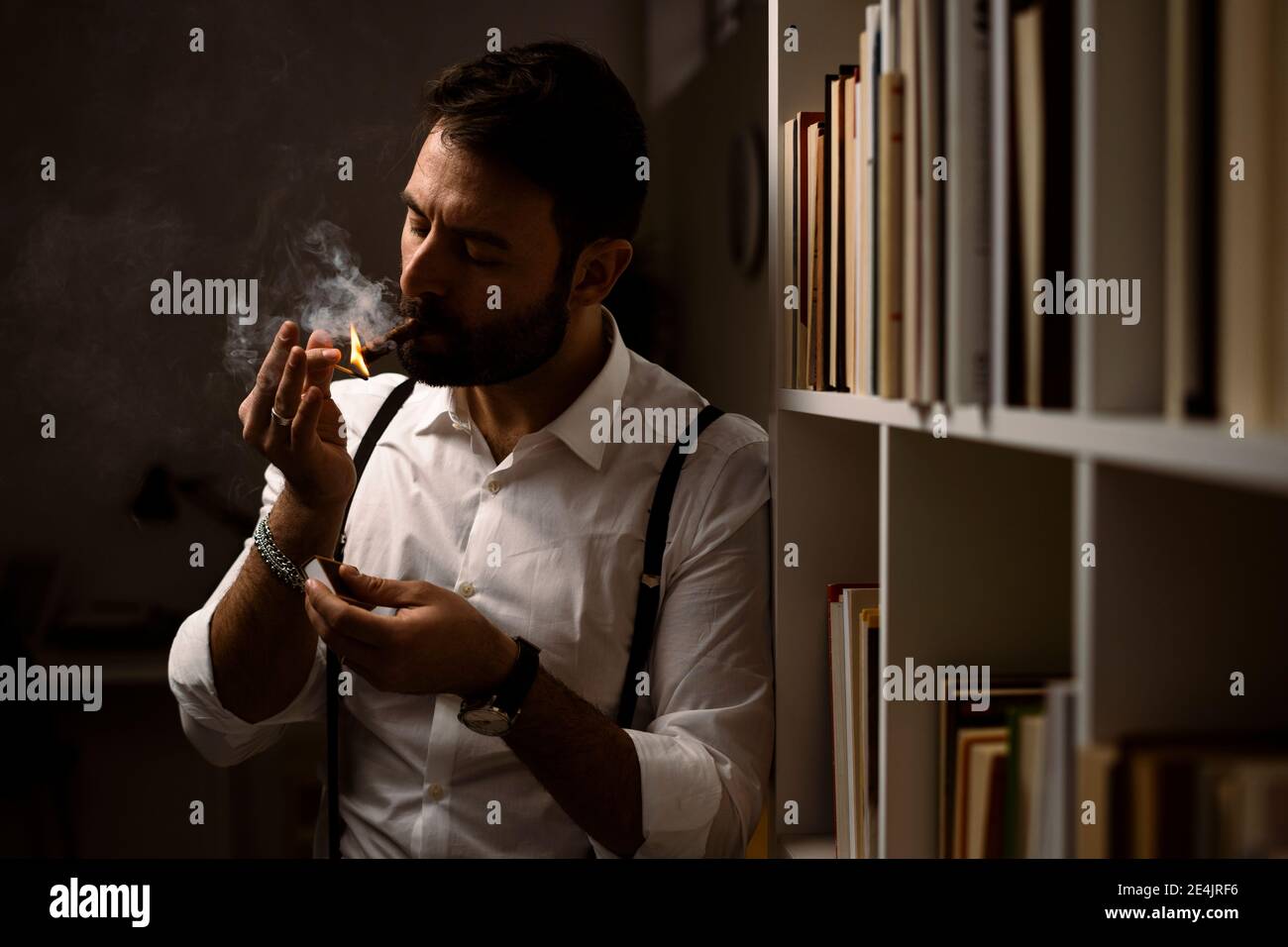 Porträt eines bärtigen Mannes, der Zigarre raucht vor dem Bücherregal Stockfoto