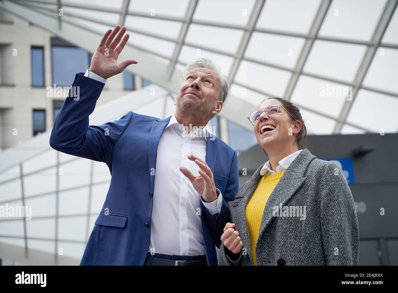 Geschäftsmann gestikuliert zu fröhlichen weiblichen Kollegen beim Blick nach oben in Stadt Stockfoto