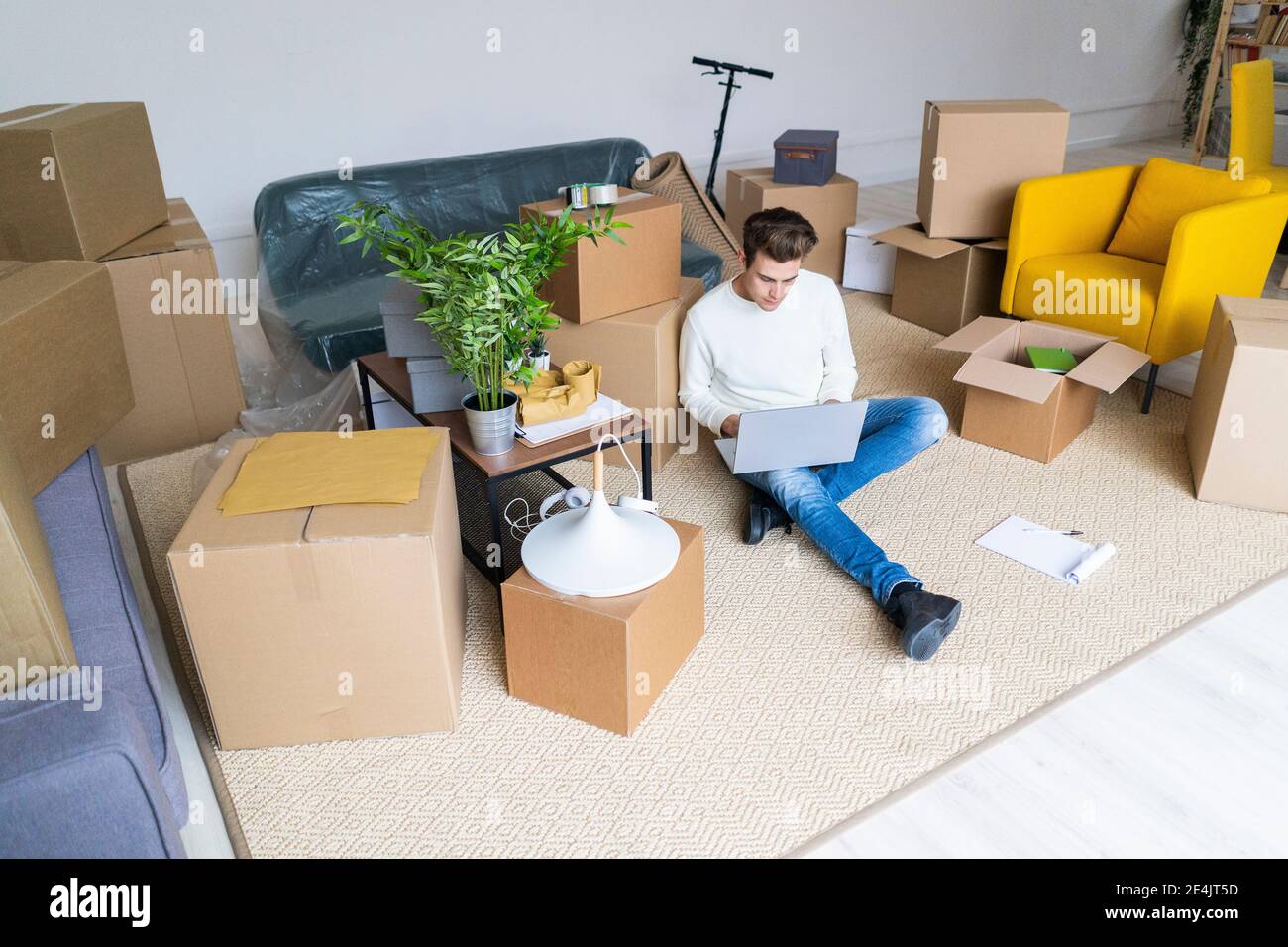 Junge viele mit Laptop in chaotisch Wohnzimmer während der Bewegung In neuem Zuhause Stockfoto