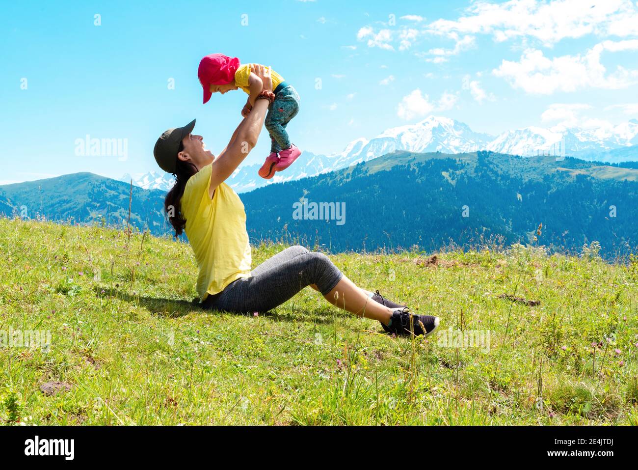 Verspielte Mutter mit ihrem Kind, das im Col des Aravis, Haute-Savoie, Frankreich, auf Gras spielt Stockfoto