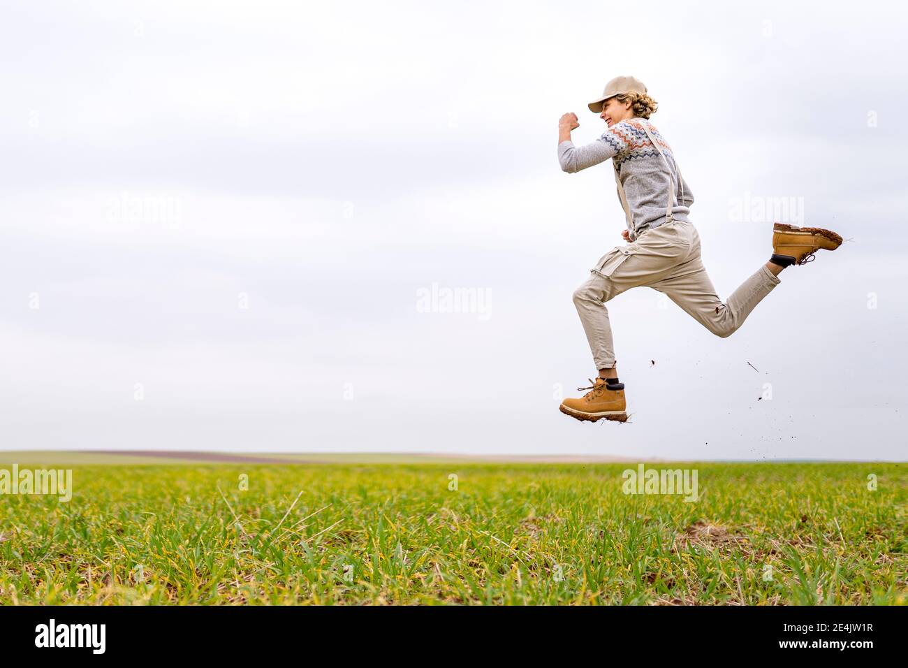 Junger Mann springt und posiert mitten in der Luft in grasbewachsenen Feld Stockfoto