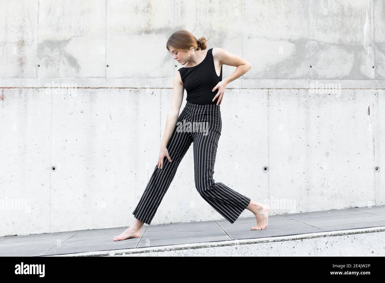 Tänzerin in schwarz gestreifter Hose vor Betonwand Stockfoto