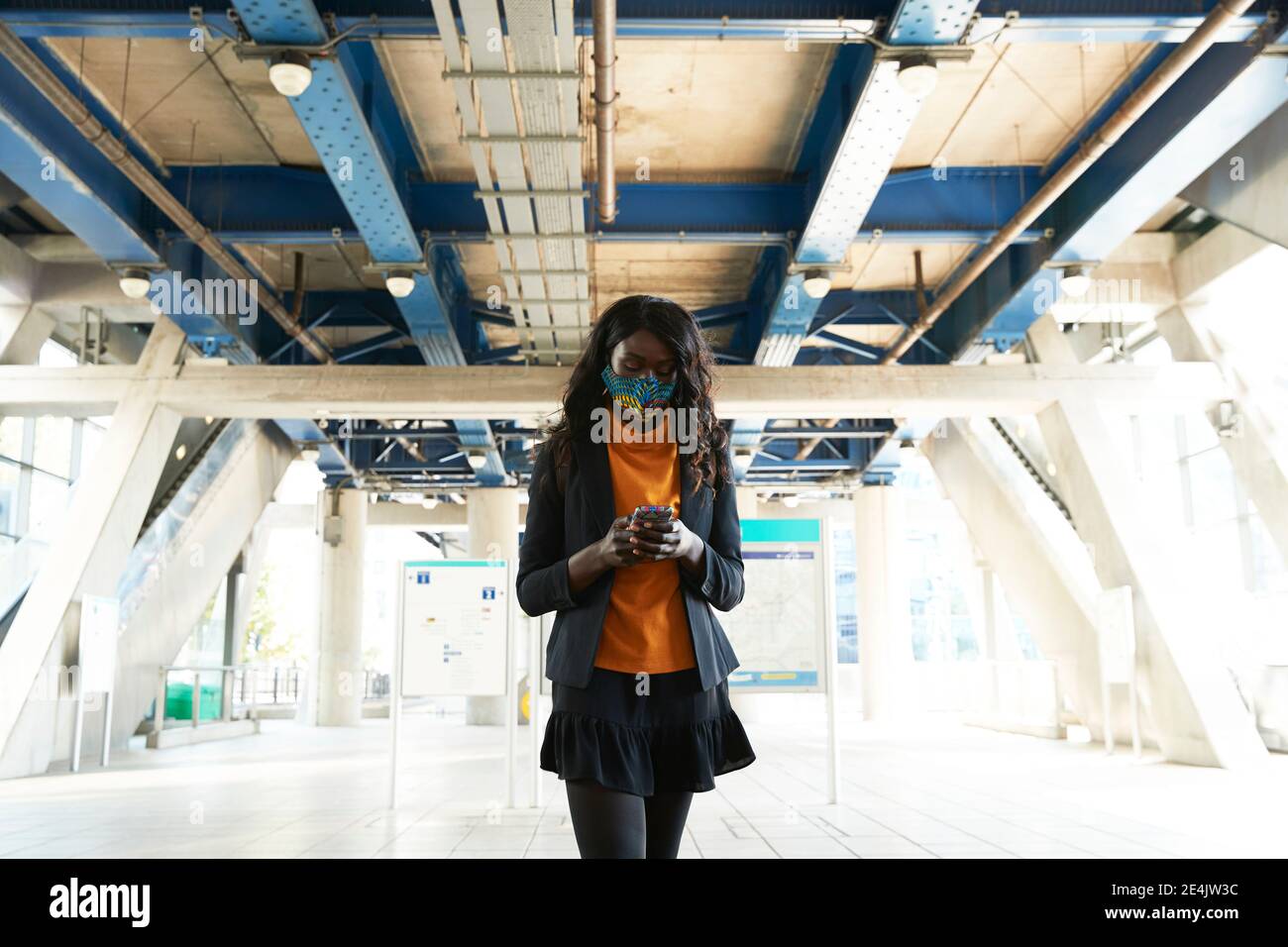 Geschäftsfrau, die während der COVID-19 unterwegs ein Mobiltelefon benutzt Stockfoto
