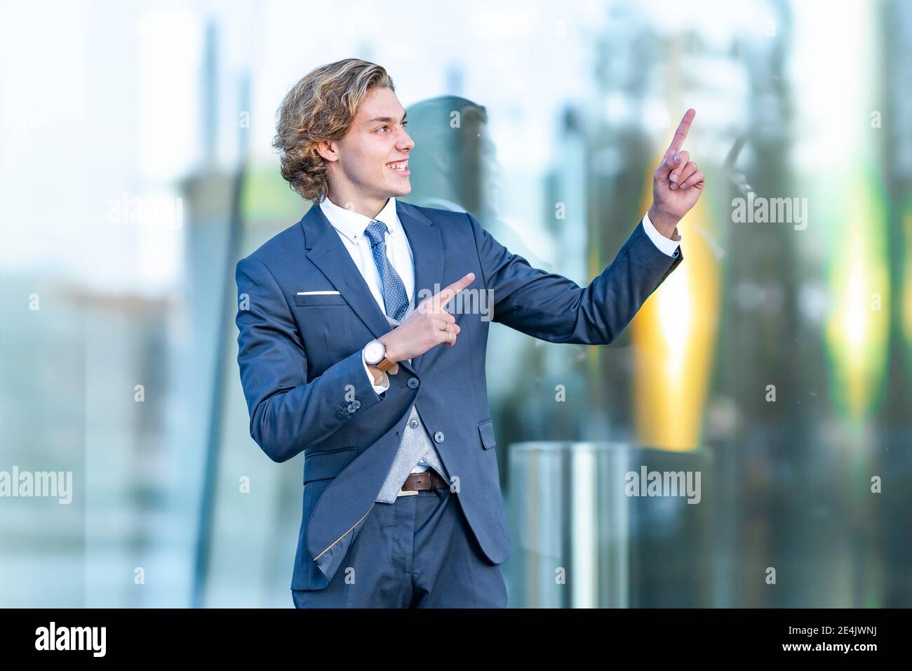 Fröhlicher junger Geschäftsmann, der gegen das gläserne Bürogebäude gestikuliert Stockfoto