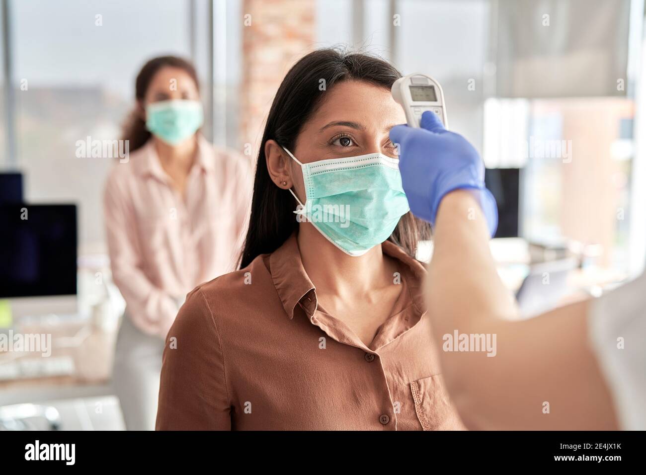 Frau mit mittlerem Erwachsenen, die die Temperatur einer Geschäftsfrau mit einem Infrarot-Thermometer im Büro überprüft Stockfoto