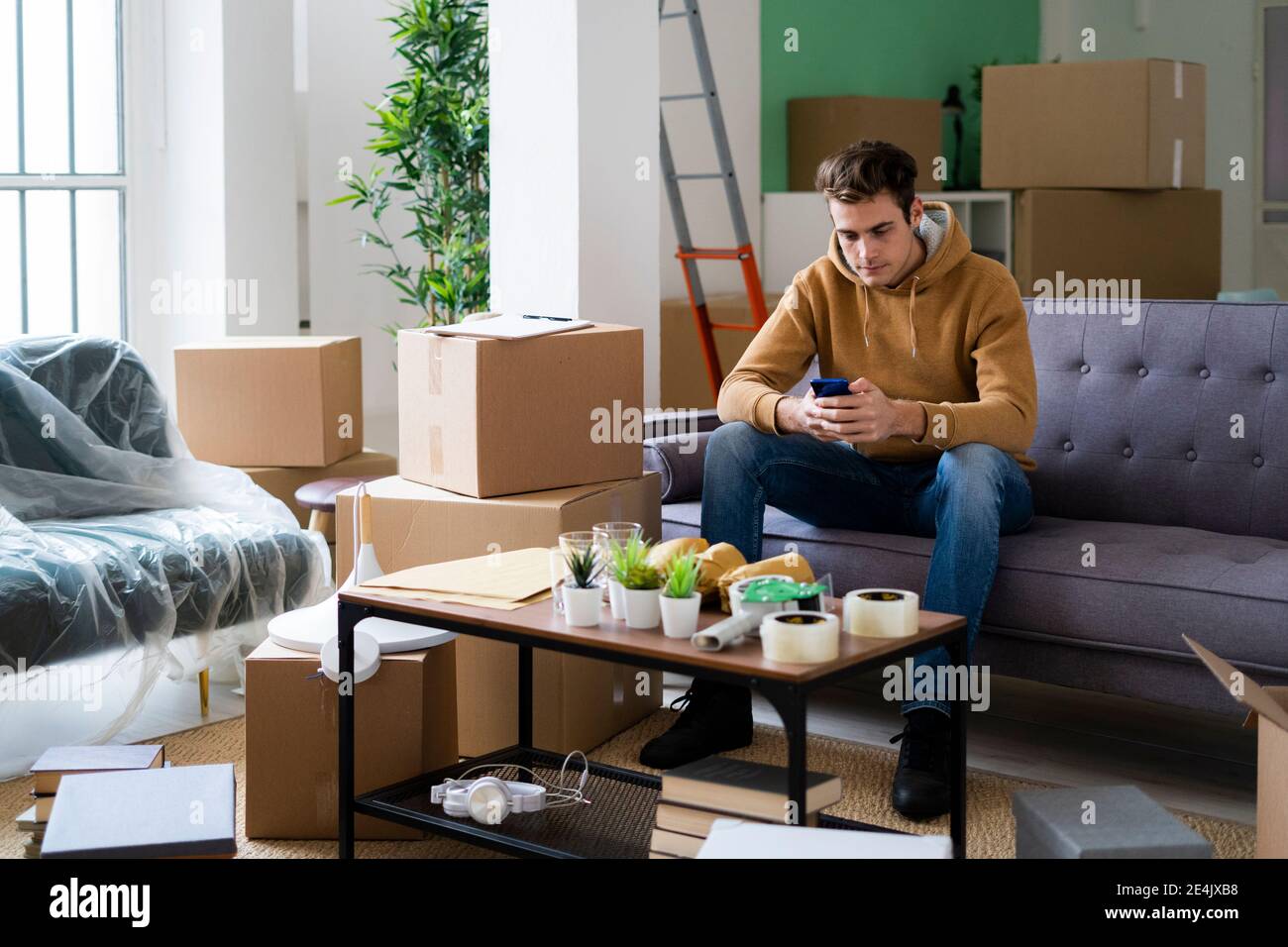 Junger Mann mit Smartphone beim Umzug in neue Loft Wohnung Stockfoto