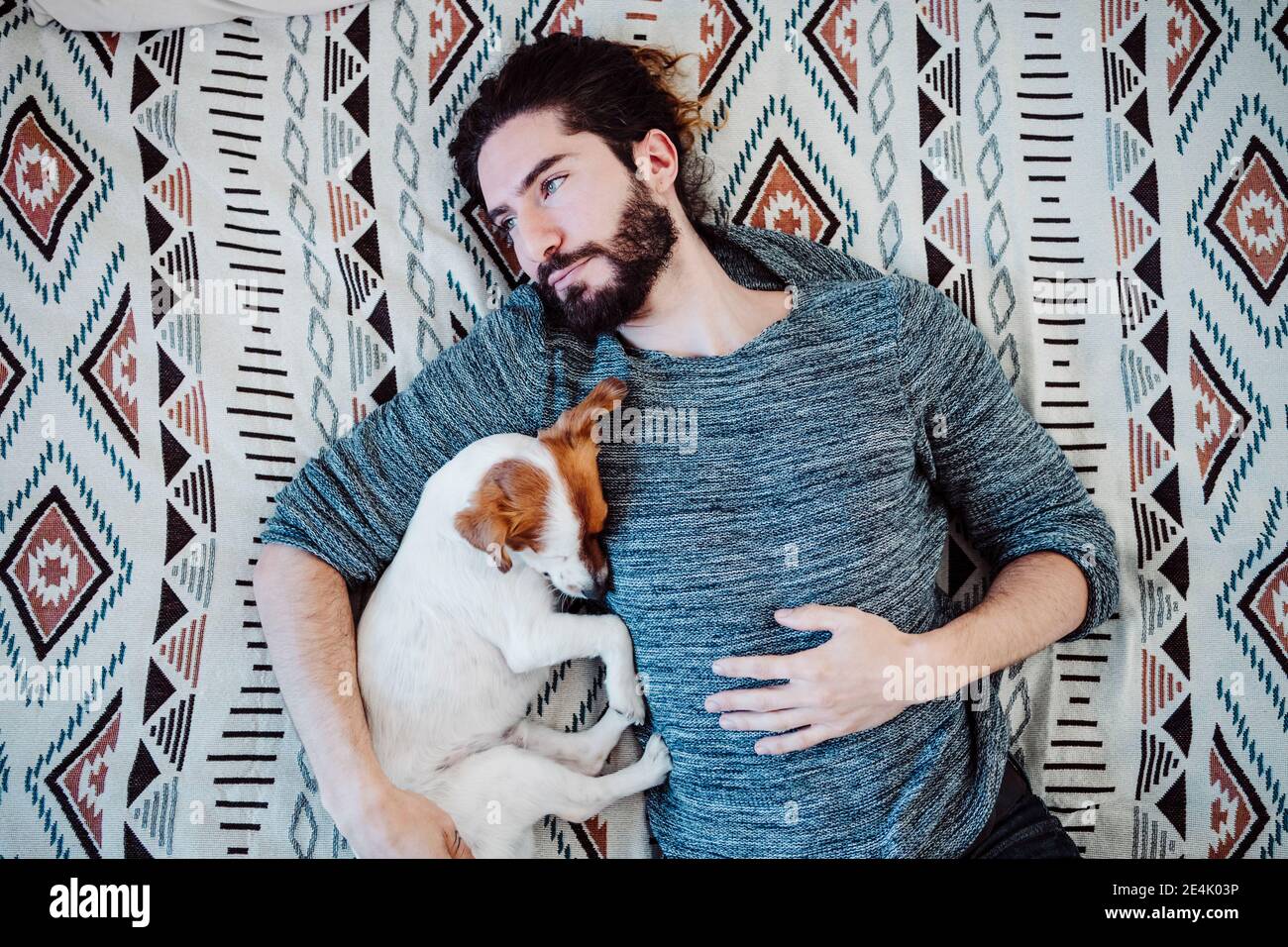 Nachdenklicher Mann, der zu Hause mit Hund auf dem Bett liegt Stockfoto