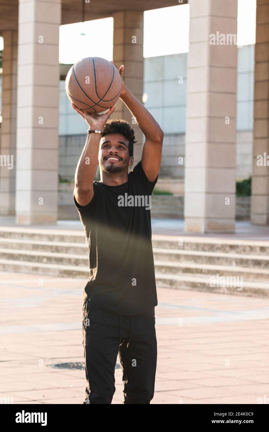 Lächelnder junger Mann, der während des Sonnenuntergangs im Park Basketball spielt Stockfoto