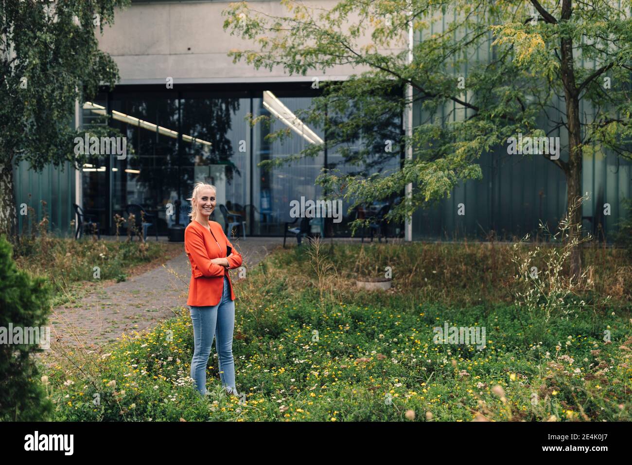 Frau mit gekreuzten Armen stehend im Firmengarten Stockfoto