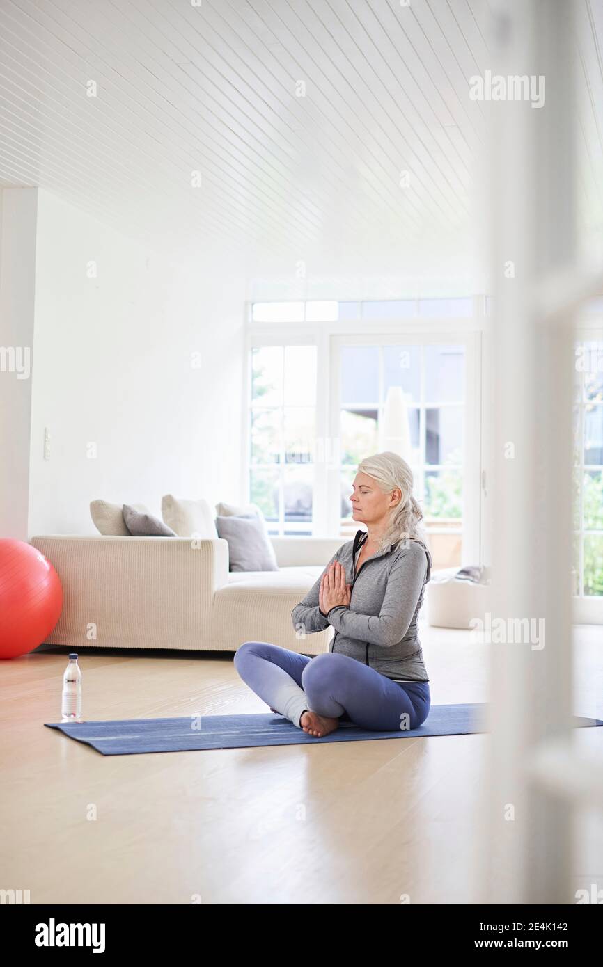 Ältere Frau mit geschlossenen Augen meditiert im Wohnzimmer Stockfoto