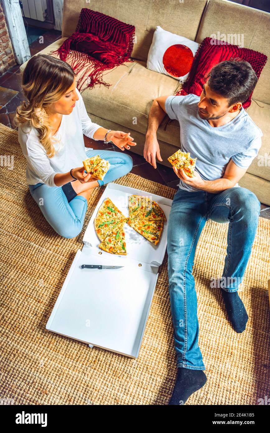 Junges Paar, das auf dem Boden des Wohnzimmers sitzt und isst Pizza aus der Box Stockfoto