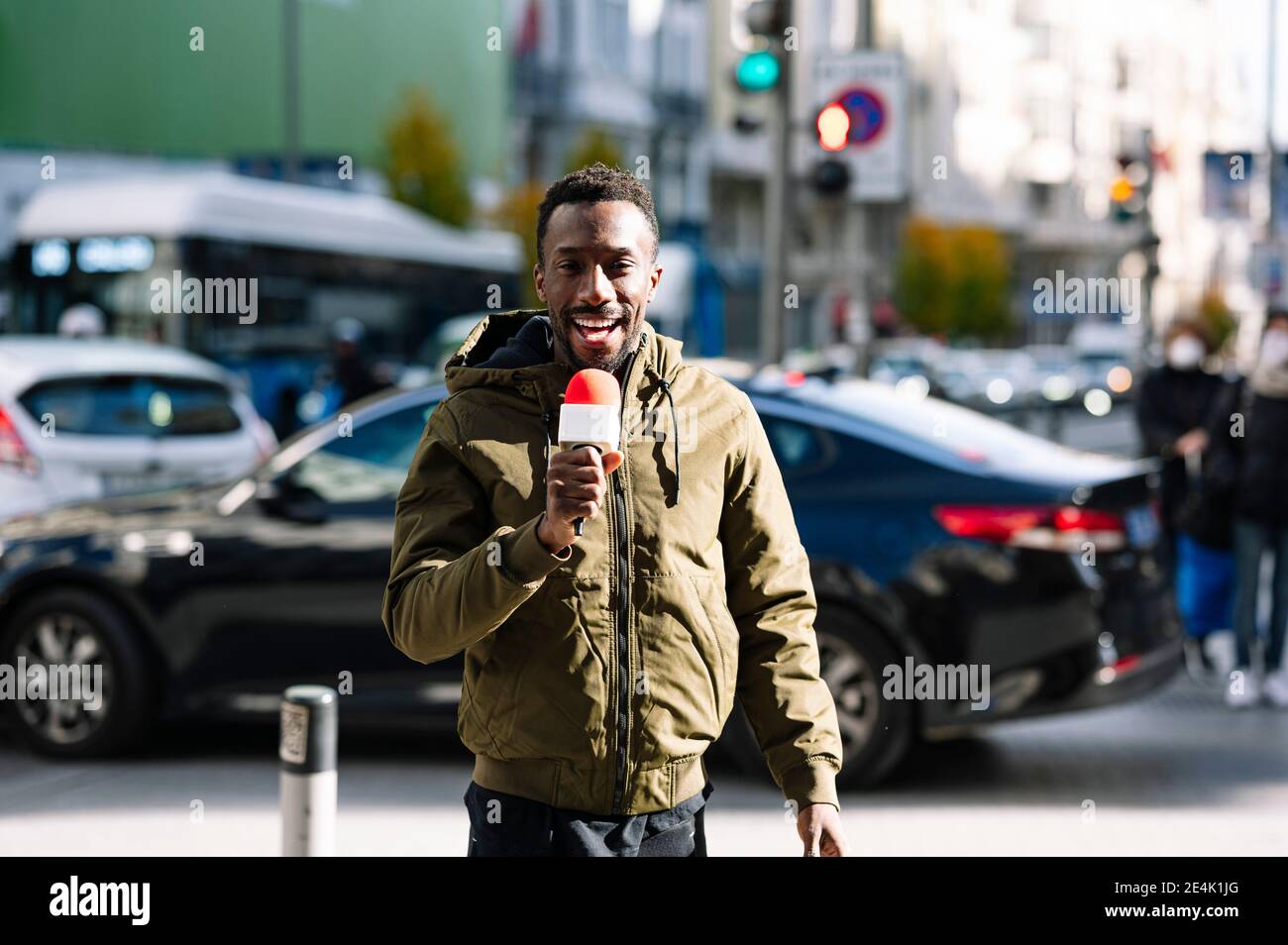 Männlicher Fernsehreporter, der über das Mikrofon spricht, während er auf der Straße steht Stockfoto
